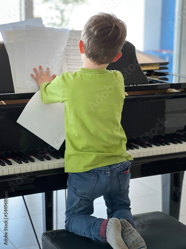 Rear view of boy holding sheet music on piano