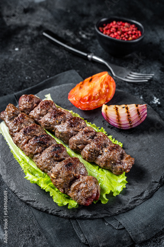 Grilled Urfa kebab with tomato, salad and onion. Black background. Top view