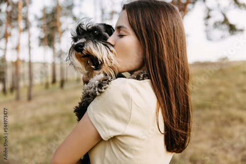 Obraz na płótnie Young brunette woman hugging a miniature schnauzer breed dog, kissing it