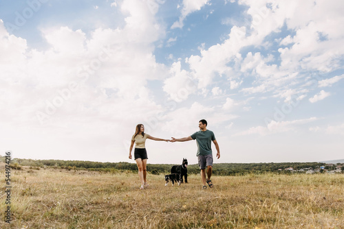 Couple of man and woman walking in an open field with two dogs.