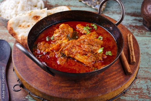 Traditional spicy Indian chicken Madras curry Rogan Josh with drumsticks, wings and garlic chapati bread served as close-up in a saucepan photo