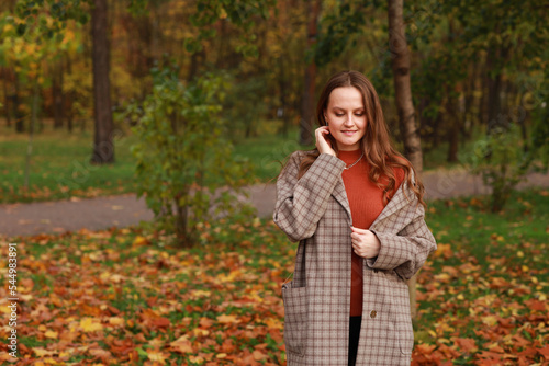Beautiful woman in jacket holding hands near head in autumn park