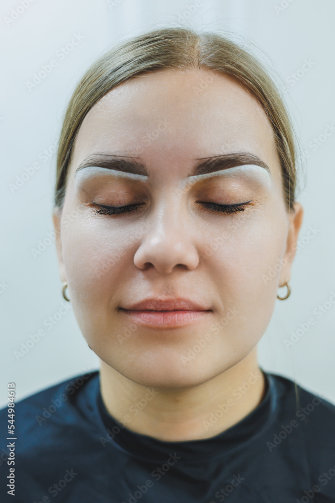 A woman permanent makeup artist draws a sketch of the eyebrows on the face of her client. A woman permanent makeup artist draws a sketch of the eyebrows on the face of her client.