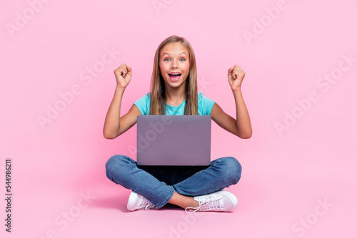 Full length photo of lucky excited small kid wear turquoise t-shirt rising fists chatting modern device isolated pink color background © deagreez