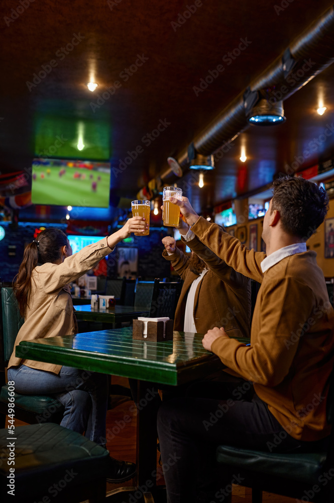Friends watching football match clinking beer mug rest in sport bar - obrazy, fototapety, plakaty 