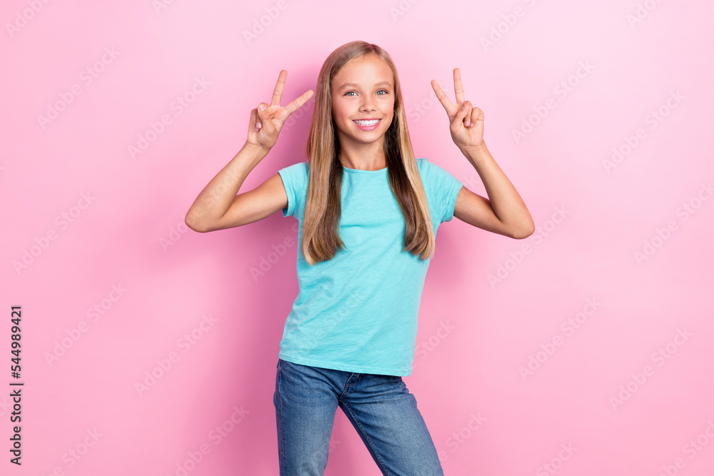 Photo of charming small schoolgirl kid wear aquamarine t-shirt showing two v-sign symbol positive enjoy good mood posing isolated on pastel pink color background Photo of charming small schoolgirl kid wear aquamarine t-shirt showing two v-sign symbol positive enjoy good mood posing isolated on pastel pink color background