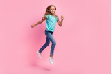 Full length photo of excited sweet small kid wear turquoise t-shirt running fast jumping high isolated pink color background