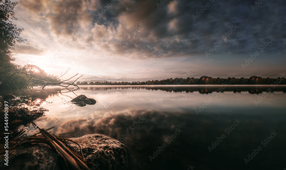 Obraz premium Sonnenaufgang am See mit vielen Reflektionen und einem dramatischen Wolken-Himmel