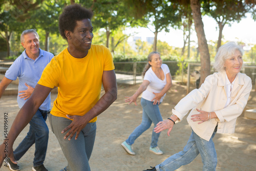 Positive multiracial mature casual pensioners practicing group dancing while enjoying sunshine weather outdoors in autumn © JackF