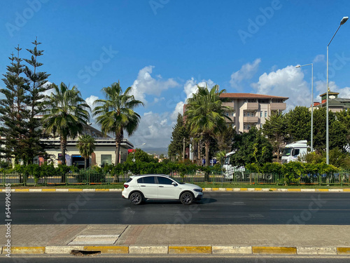 White car and beautiful modern buildings, architecture, road and palm trees in a warm tropical oriental southern country resort © Aliaksandra