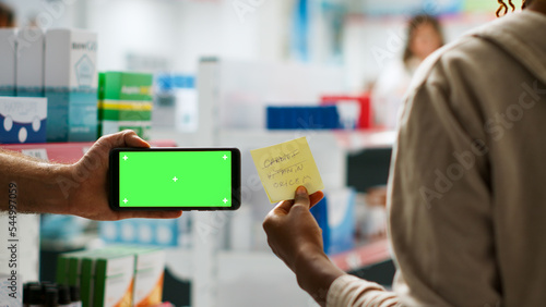 Modern smartphone showing horizontal greenscreen template in medical drugstore, isolated display with chroma key on mobile phone. Blank mockup background on telephone in pharmacy. Tripod shot.