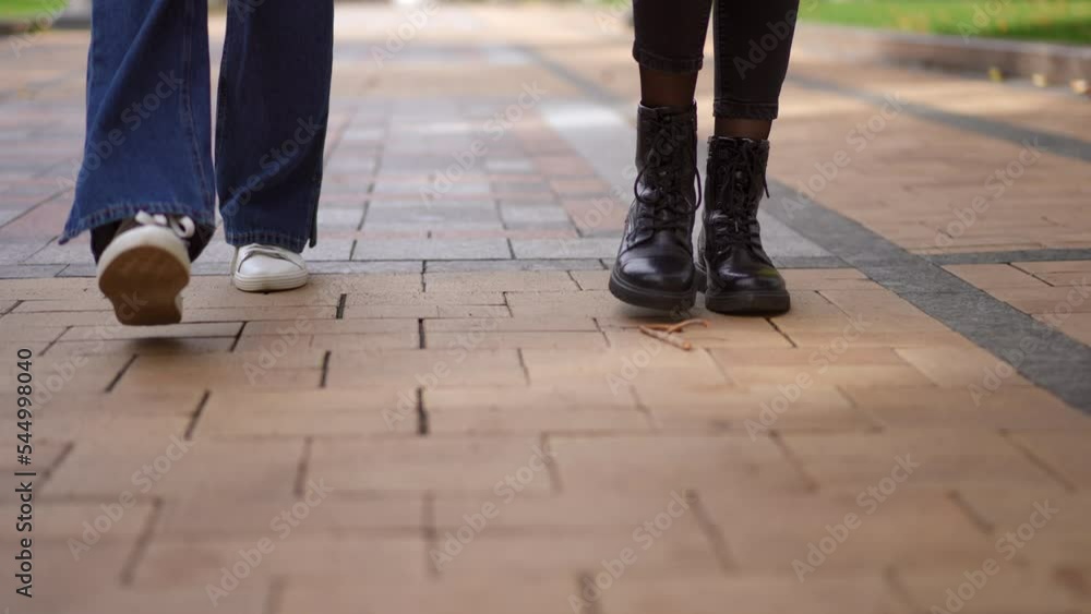 Front view steps of two unrecognizable women strolling along pavement alley in city park. Unrecognizable Caucasian friends walking outdoors. Lifestyle concept Front view steps of two unrecognizable women strolling along pavement alley in city park. Unrecognizable Caucasian friends walking outdoors. Lifestyle concept