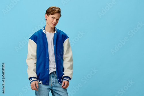 Fotografia a happy guy in a white t-shirt and a trendy teen bomber jacket stands smiling looking at the camera on a plain background with space for text