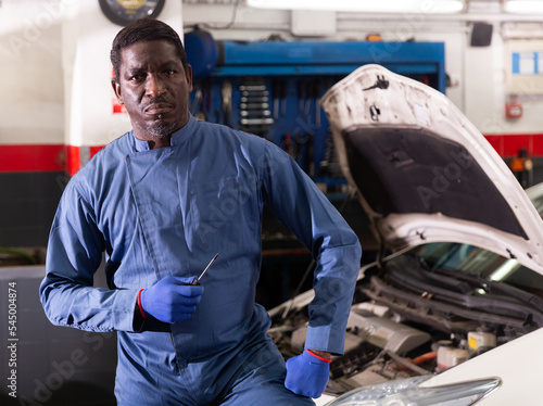 Portrait of confident african male mechanician posing near car on his workplace in workshop