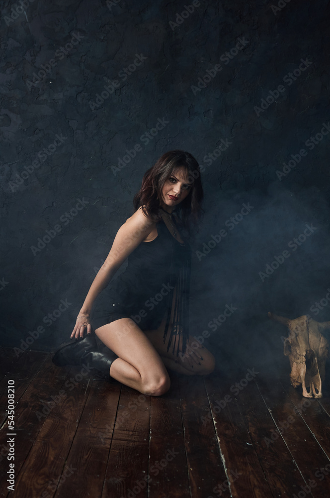 A brunette girl dressed in black shorts and a T-shirt, shod in boots, sits on the floor near a dark blue wall, dances and moves her arms. Creative state, mood to listen to music. Gothic brutal. A brunette girl dressed in black shorts and a T-shirt, shod in boots, sits on the floor near a dark blue wall, dances and moves her arms. Creative state, mood to listen to music. Gothic brutal.