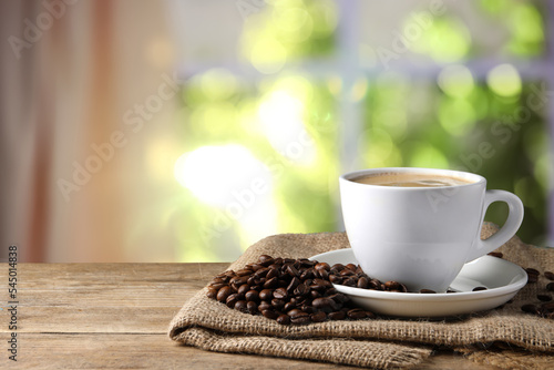 Cup of hot aromatic coffee and roasted beans on wooden table indoors  space for text