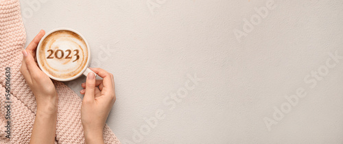 Female hands with cup of hot coffee and figure 2023 on light background with space for text photo