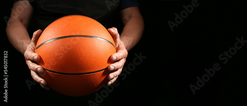 Basketball player holding rubber ball on dark background with space for text