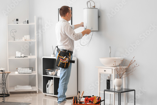 Male plumber repairing electric boiler in bathroom