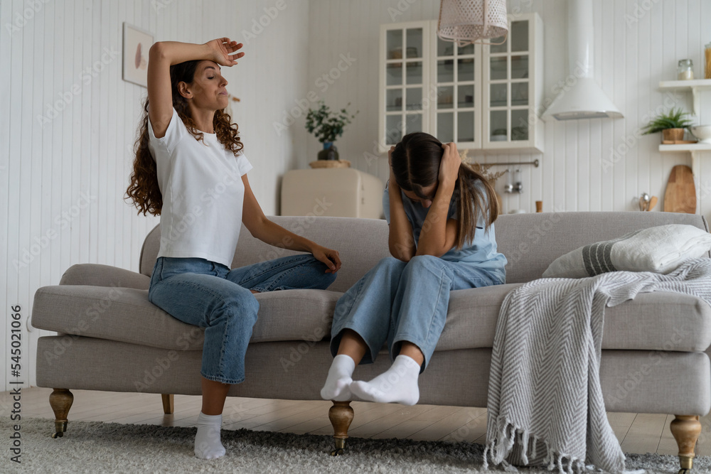 Obraz premium Communication problems between parents and teens. Exhausted parent can not deal with teenage daughter attitude, parental burnout. Teen girl covering ears with hands not to listen mom, sitting on sofa