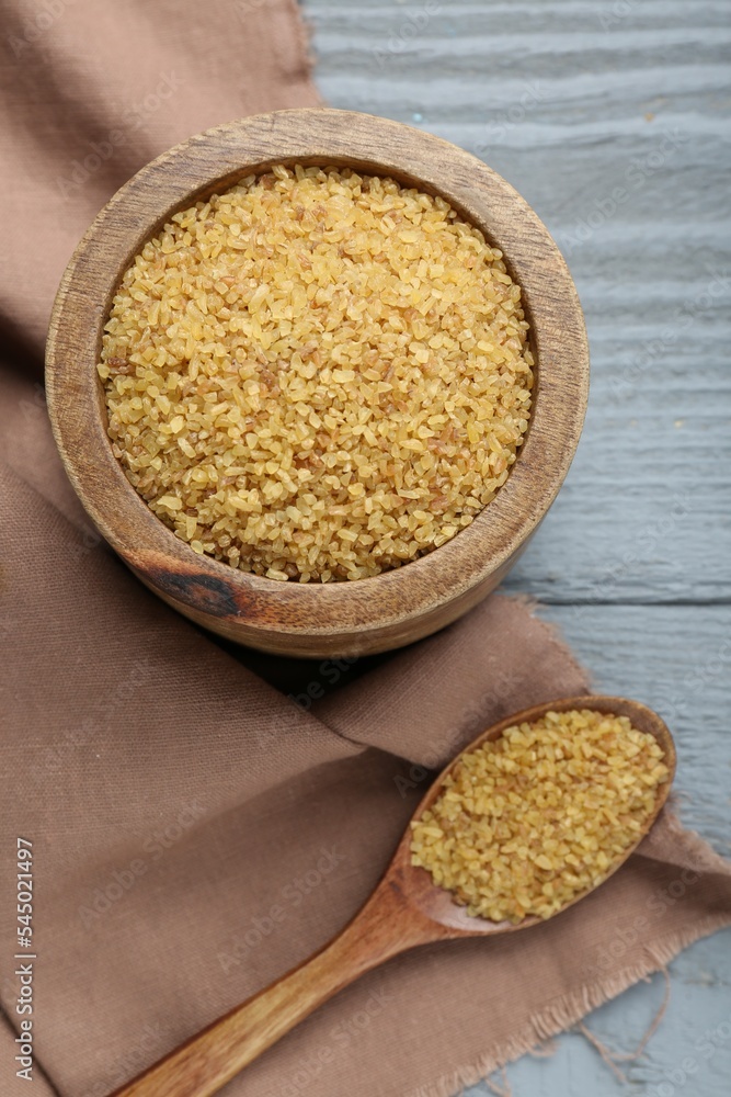 Bowl and spoon with uncooked bulgur on grey wooden table, flat lay Bowl and spoon with uncooked bulgur on grey wooden table, flat lay