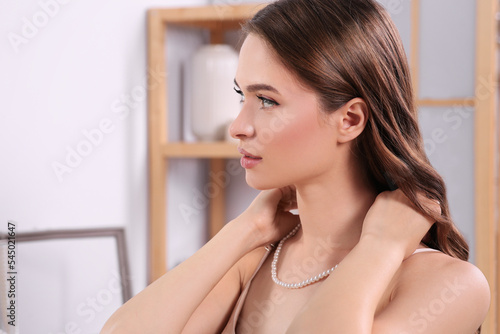 Foto Young woman trying on elegant pearl necklace indoors, space for text
