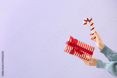 Woman with Christmas gift box and candy cane on lilac background
