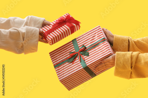 Women with Christmas gift boxes on yellow background