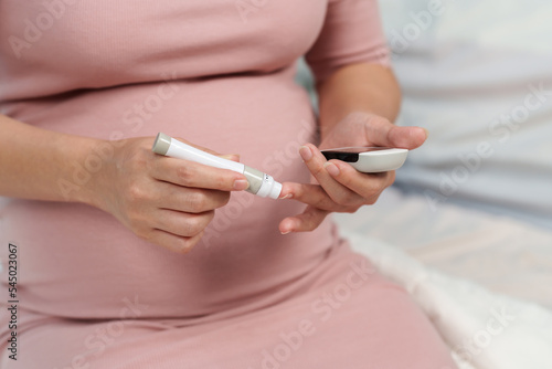 pregnant woman holding glucose meter and checking blood sugar level by herself at home. gestational diabetes concept.