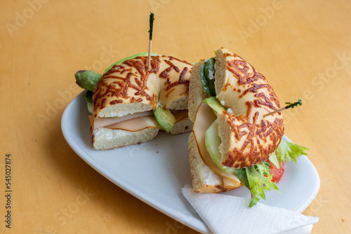 Beagle sandwich with a filling of salted chicken, arugula, cucumber, soft cheese. Beigle on kraft paper. In the background there is one more Beigle. Light background. photo