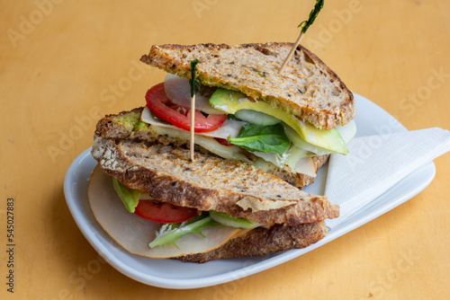 Beagle sandwich with a filling of salted chicken, arugula, cucumber, soft cheese. Beigle on kraft paper. In the background there is one more Beigle. Light background. photo