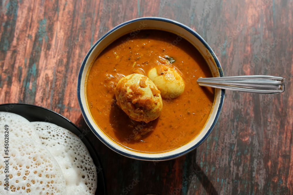 Egg roast curry or Mutta roast gravy hot and spicy dish popular spicy Kerala food with puttu appam on wooden background Tamil Nadu South India. Egg roast curry or Mutta roast gravy hot and spicy dish popular spicy Kerala food with puttu appam on wooden background Tamil Nadu South India.