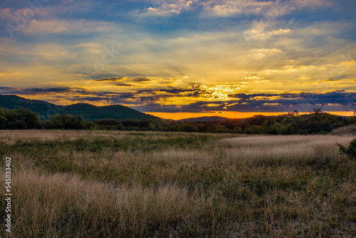 Sunrise coming over mountains behind a field of tall grass taken on the last day before the time changed in the Texas Hill Country