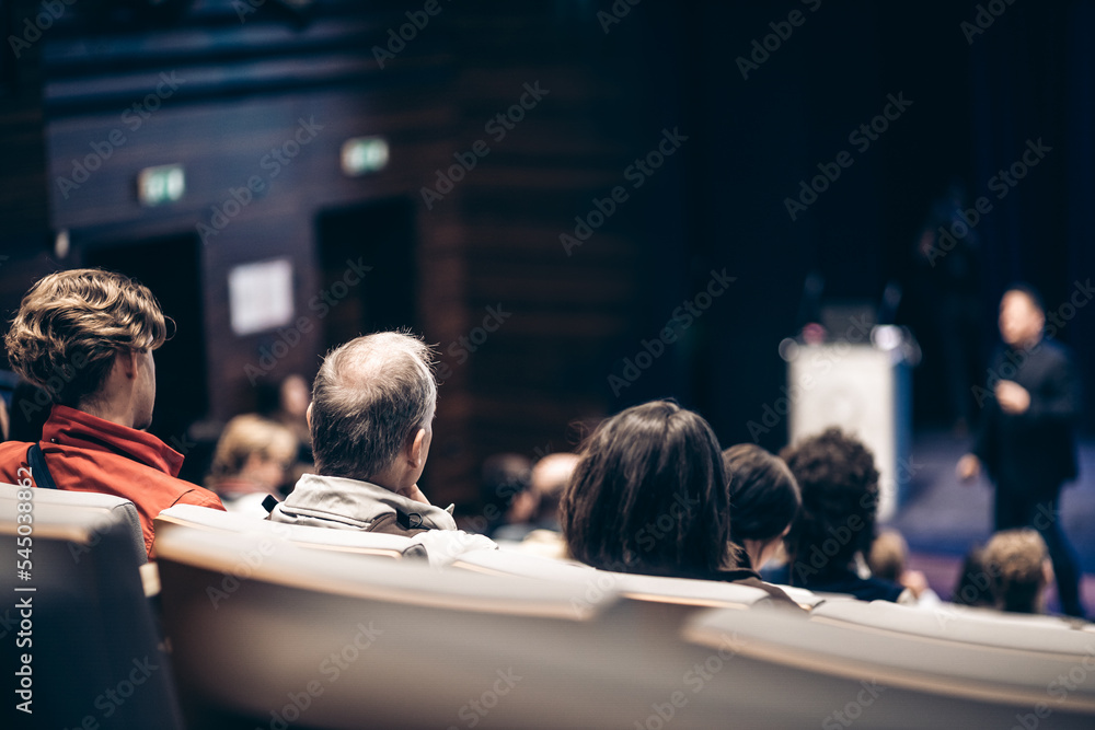 Speaker giving a talk in conference hall at business event. Rear view of unrecognizable people in audience at the conference hall. Business and entrepreneurship concept Speaker giving a talk in conference hall at business event. Rear view of unrecognizable people in audience at the conference hall. Business and entrepreneurship concept