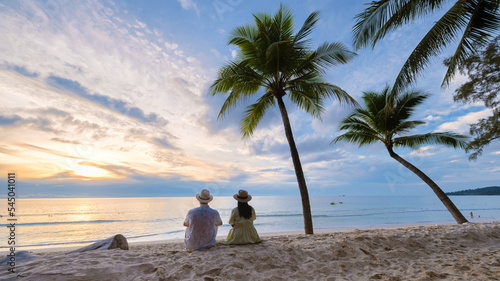 Fotografie A couple of men and women sitting on the beach watching the sunset on the beach with white sand and palm trees, Bang Tao beach Phuket Thailand