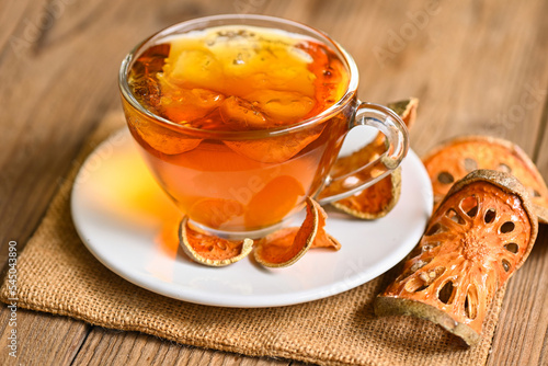Bael tea on glass with dried bael slices on wooden background, Bael juice - Dry bael fruit tea for health - Aegle marmelos