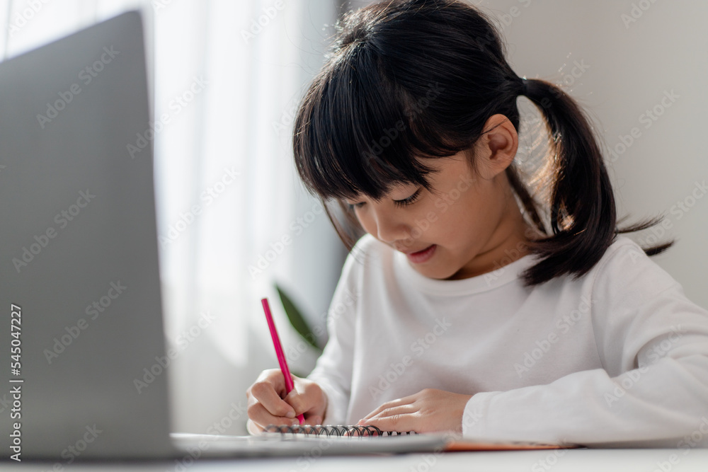 Asian schoolgirl doing her homework with laptop at home. Children use gadgets to study. Education and distance learning for kids. Homeschooling during quarantine. Stay at home Asian schoolgirl doing her homework with laptop at home. Children use gadgets to study. Education and distance learning for kids. Homeschooling during quarantine. Stay at home