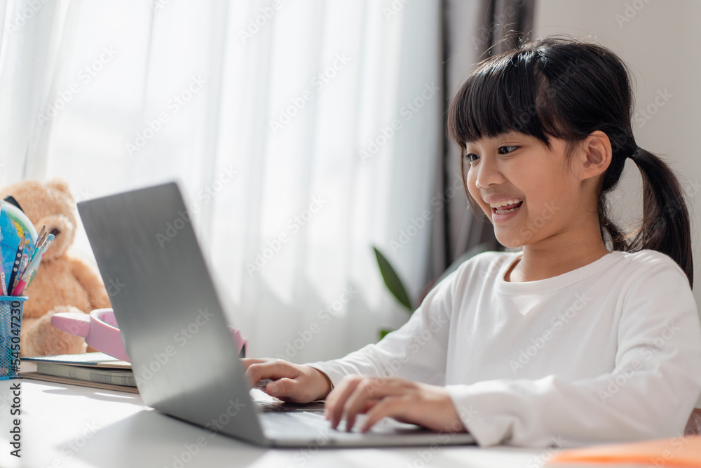 Asian schoolgirl doing her homework with laptop at home. Children use gadgets to study. Education and distance learning for kids. Homeschooling during quarantine. Stay at home Asian schoolgirl doing her homework with laptop at home. Children use gadgets to study. Education and distance learning for kids. Homeschooling during quarantine. Stay at home