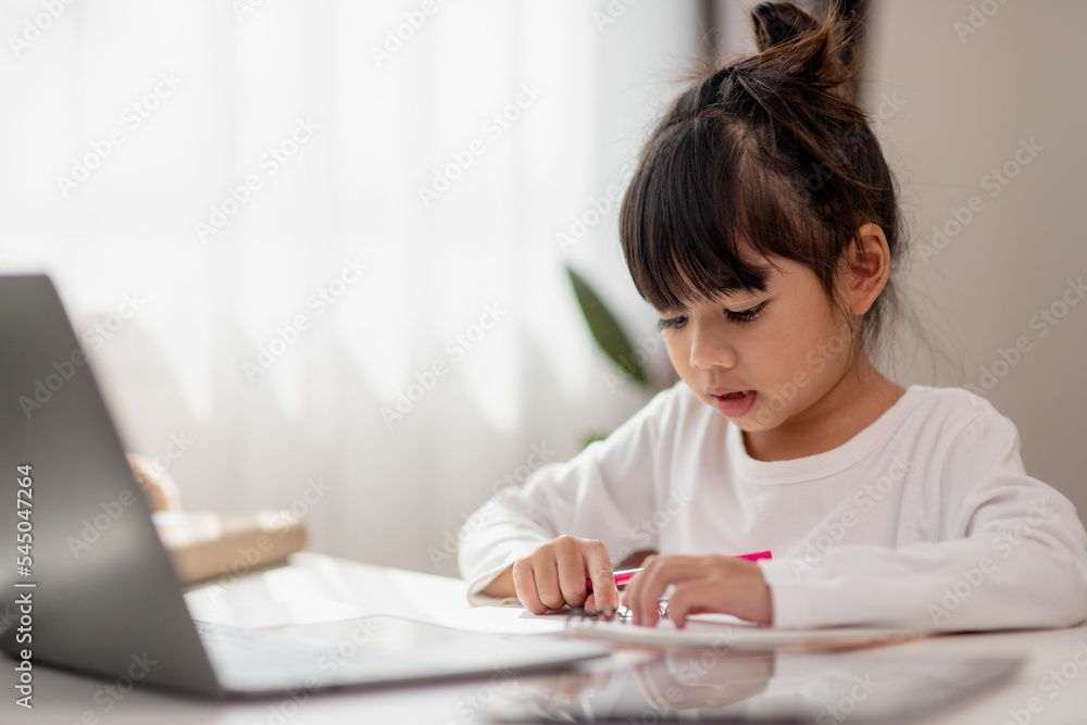 Asian schoolgirl doing her homework with laptop at home. Children use gadgets to study. Education and distance learning for kids. Homeschooling during quarantine. Stay at home Asian schoolgirl doing her homework with laptop at home. Children use gadgets to study. Education and distance learning for kids. Homeschooling during quarantine. Stay at home