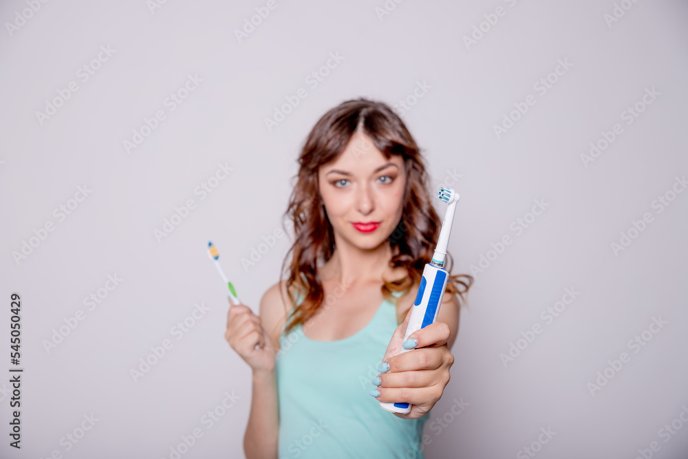 Young woman undecided whether to use the electric or traditional toothbrush, isolated on white background.Oral hygiene and health care. Dentistry.Electric and classical toothbrush Young woman undecided whether to use the electric or traditional toothbrush, isolated on white background.Oral hygiene and health care. Dentistry.Electric and classical toothbrush
