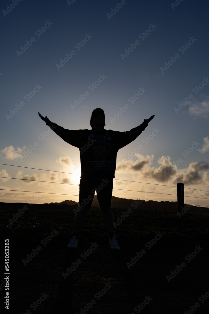 Fototapeta premium Silhouette of a man posing with hands wide open with the sun setting in the background from a group-up view