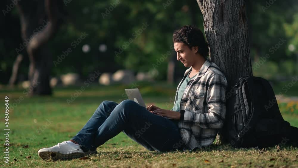 Smiling mixed race casual student guy e learning remotely use laptop outdoor at summer sunny park Smiling mixed race casual student guy e learning remotely use laptop outdoor at summer sunny park