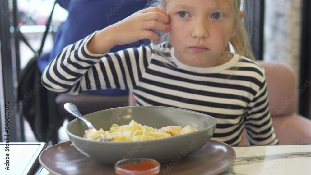 A hungry child eats homemade pasta with ketchup and chews gum in the summer at a restaurant. A hungry child eats homemade pasta with ketchup and chews gum in the summer at a restaurant.