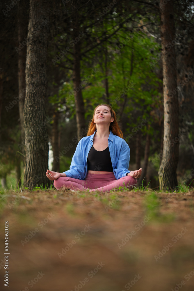 Redhead young woman meditating in a forest. Meditation in nature. Redhead young woman meditating in a forest. Meditation in nature.