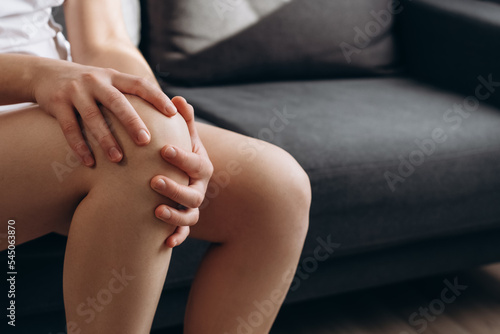 Wallpaper Mural Close up side view unhealthy young female suffering from pain knee, does massage itself sitting on couch at home. Trauma or torn ligament. Concept medical, people and physiotherapy due to knee pain Torontodigital.ca