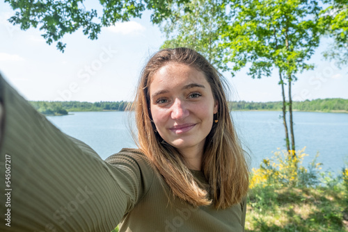 Beautiful young brunette Caucasian woman taking a selfie with smartphone outdoors on a forest lake in spring. High quality photo photo