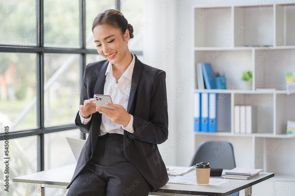 Young beautiful asian woman using smartphone and working with laptop while sitting at office desk, working from home concept. Young beautiful asian woman using smartphone and working with laptop while sitting at office desk, working from home concept.