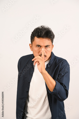 Portrait of Young asian man in blue shirt asking to be quiet with finger on lips isolated on white background