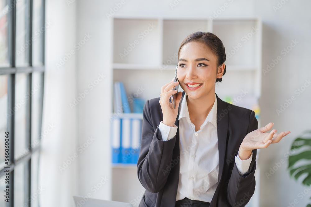 Young beautiful asian woman using smartphone and working with laptop while sitting at office desk, working from home concept. Young beautiful asian woman using smartphone and working with laptop while sitting at office desk, working from home concept.