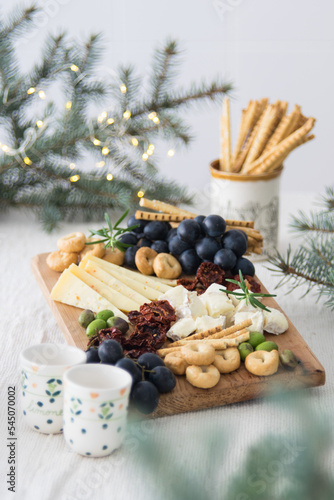 Cheese plate served with grapes, olives, crackers and dried tomatoes on a wooden background with new year lights, selective focus